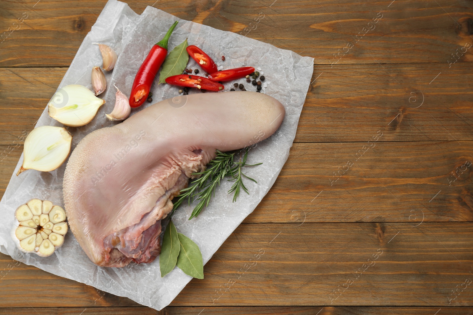 Photo of Parchment with raw beef tongue and products on wooden table, top view. Space for text