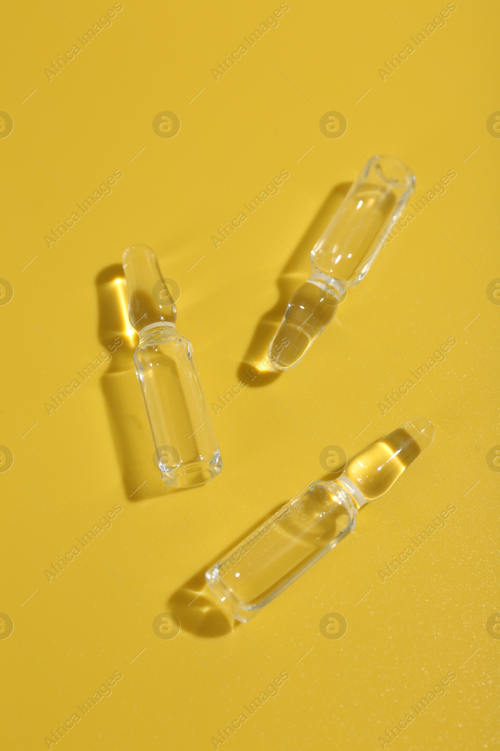 Photo of Glass ampoules with liquid on yellow background, flat lay