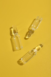 Photo of Glass ampoules with liquid on yellow background, flat lay