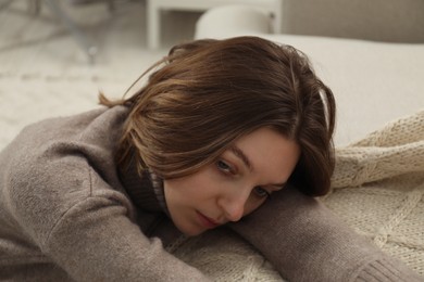 Sad young woman sitting near sofa at home