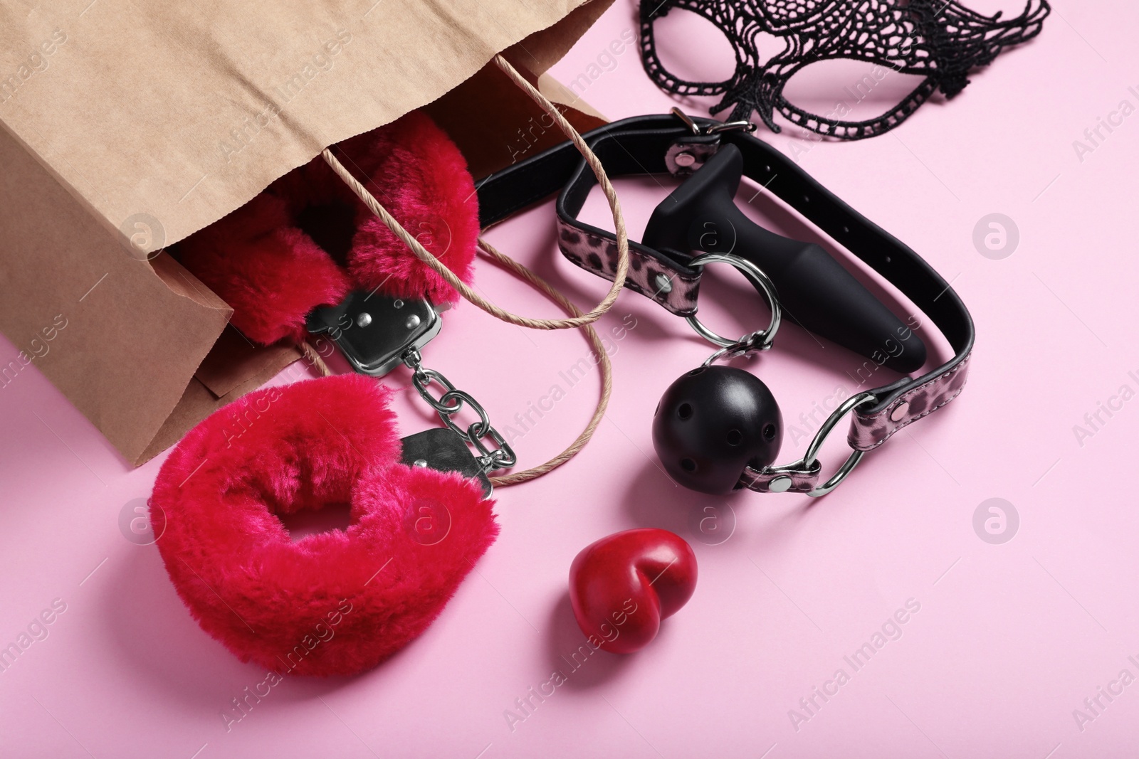 Photo of Paper shopping bag with different sex toys on pink background