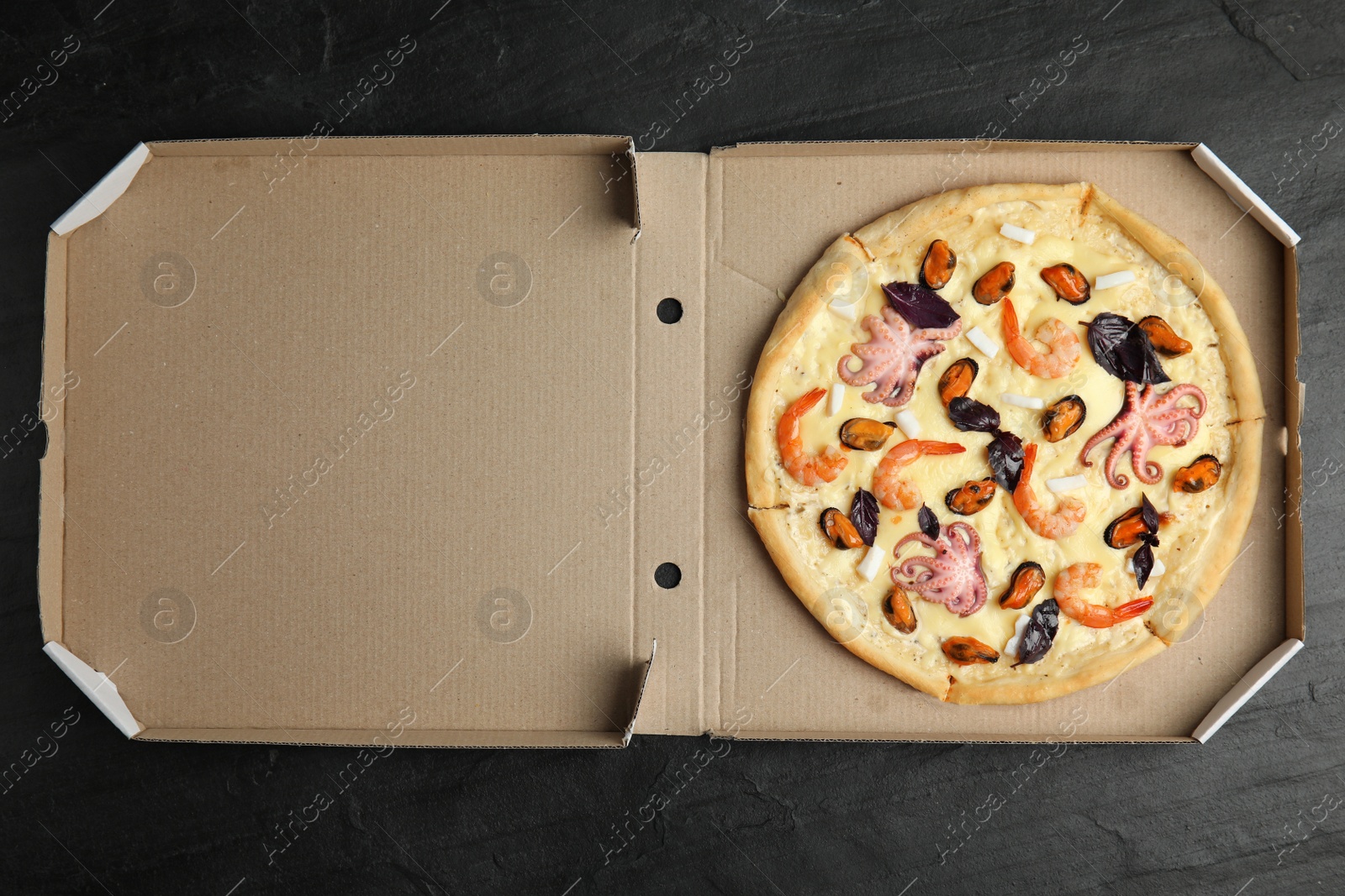 Photo of Delicious seafood pizza in cardboard box on black table, top view