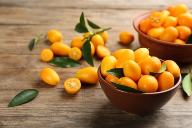 Fresh ripe kumquats in bowl on wooden table, space for text