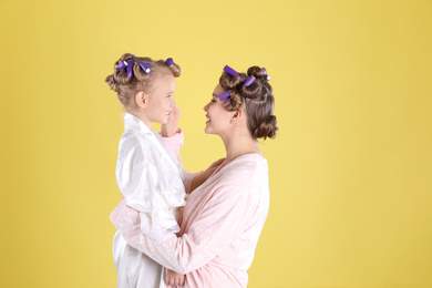 Photo of Happy mother and daughter with curlers on yellow background