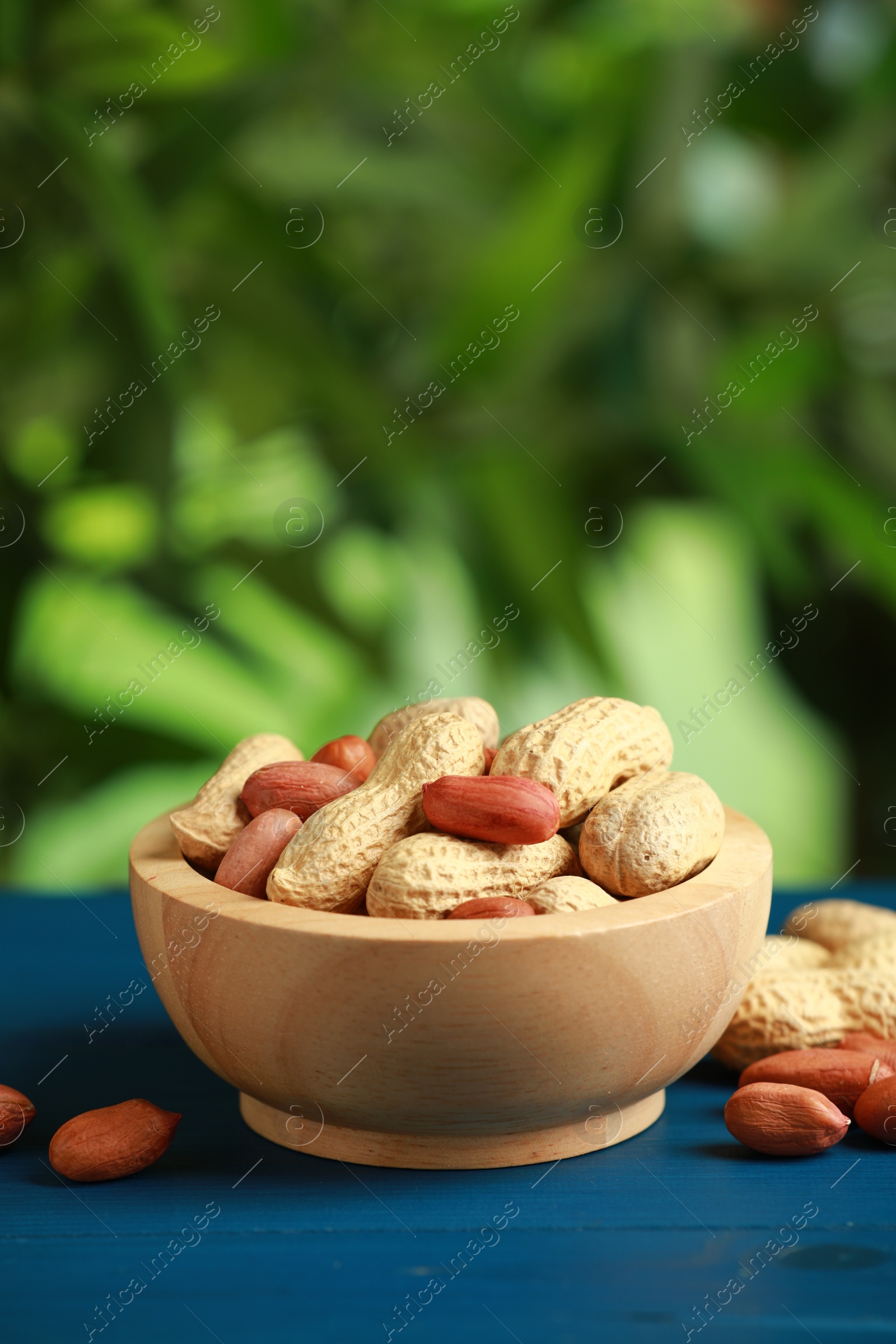 Photo of Fresh unpeeled peanuts in bowl on blue wooden table against blurred background