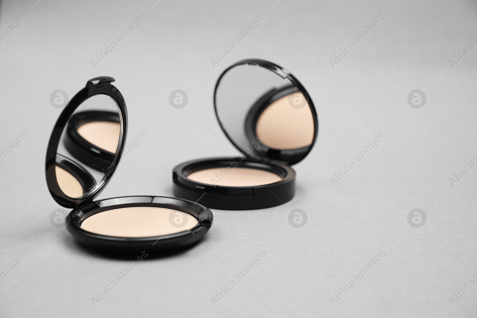 Photo of Open face powders with mirrors on light grey background. Space for text