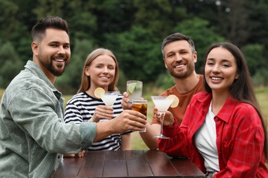 Photo of Happy friends holding glasses with cocktails at table outdoors