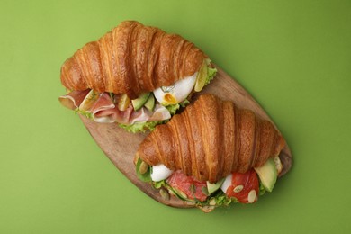 Photo of Delicious croissants with prosciutto and salmon on green table, top view