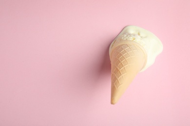 Photo of Melted vanilla ice cream in wafer cone on pink background, above view. Space for text
