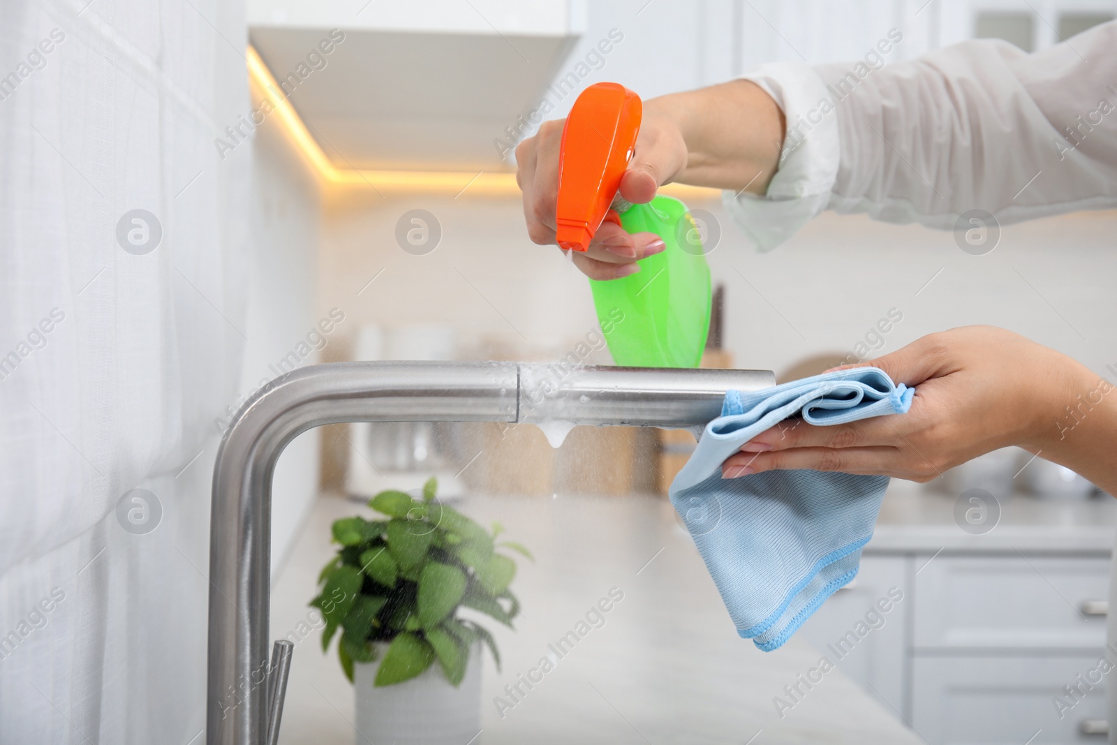 Photo of Woman cleaning tap with rag and detergent in kitchen, closeup