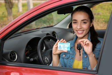 Happy woman showing driving license and key from new car