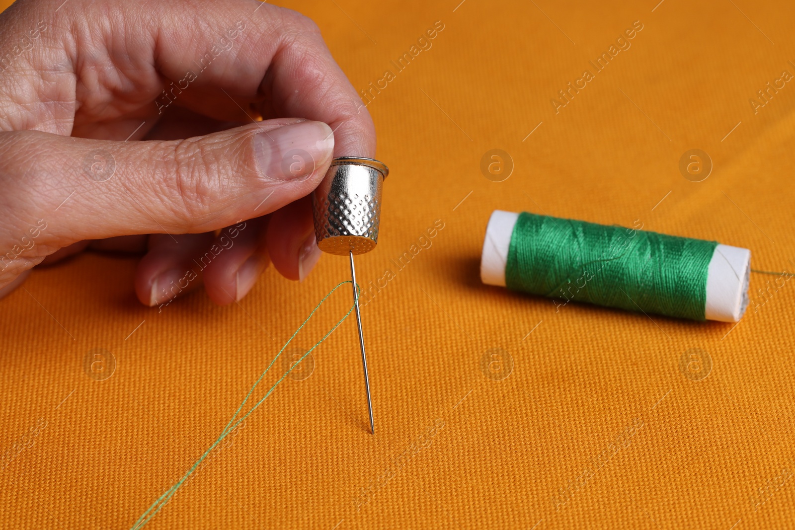 Photo of Woman sewing on orange fabric with thimble and needle, closeup