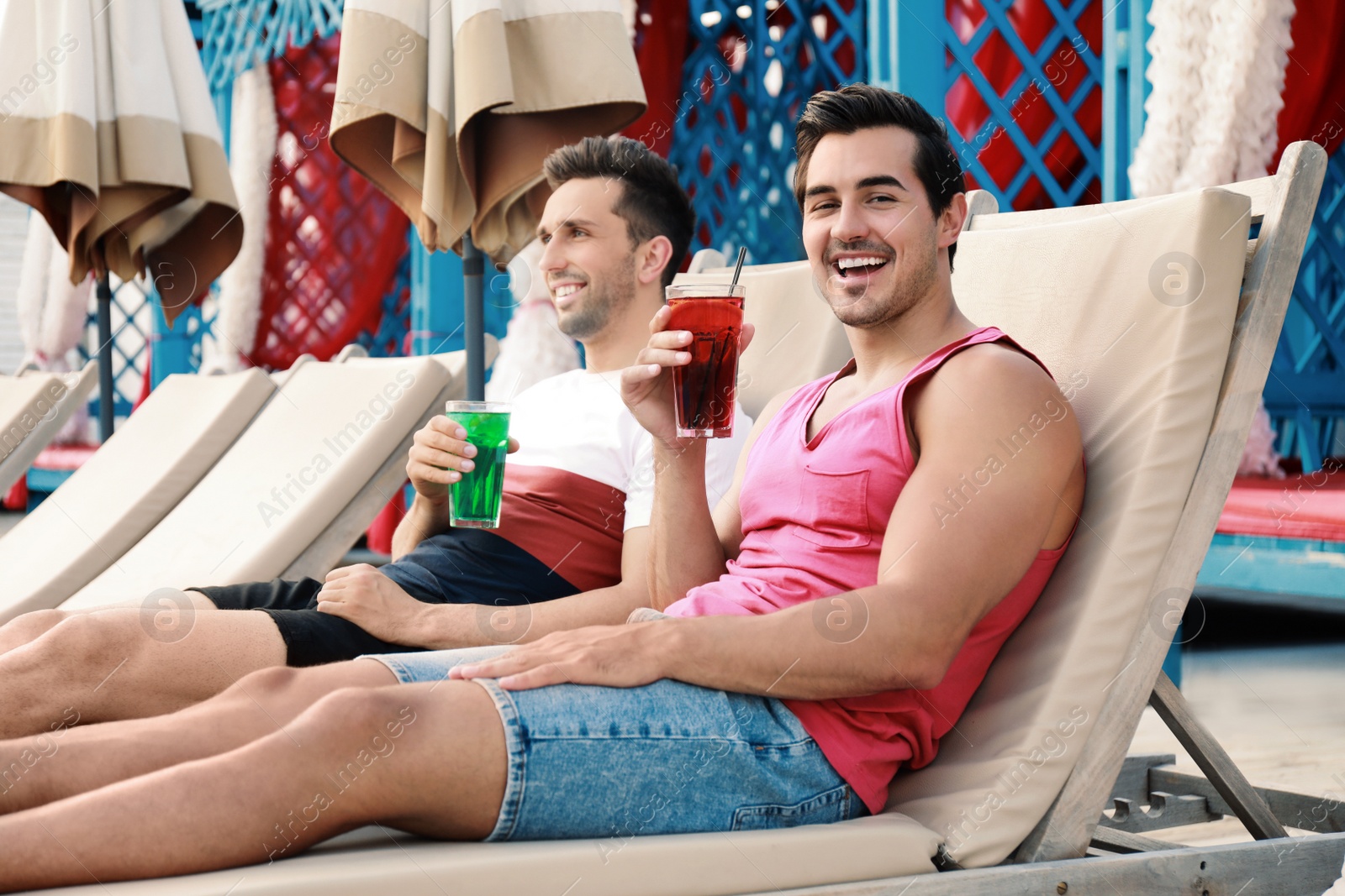 Photo of Happy young friends with fresh summer cocktails relaxing on sunbeds