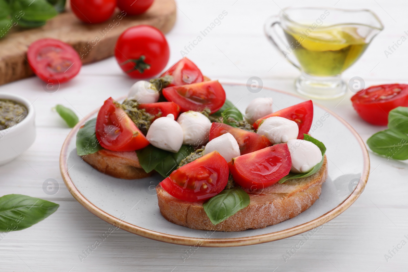 Photo of Delicious Caprese sandwiches with mozzarella, tomatoes, basil and pesto sauce on white wooden table