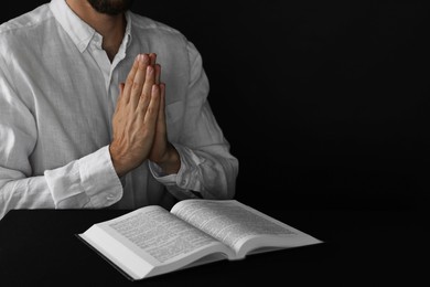 Photo of Man with Bible praying at black table, closeup