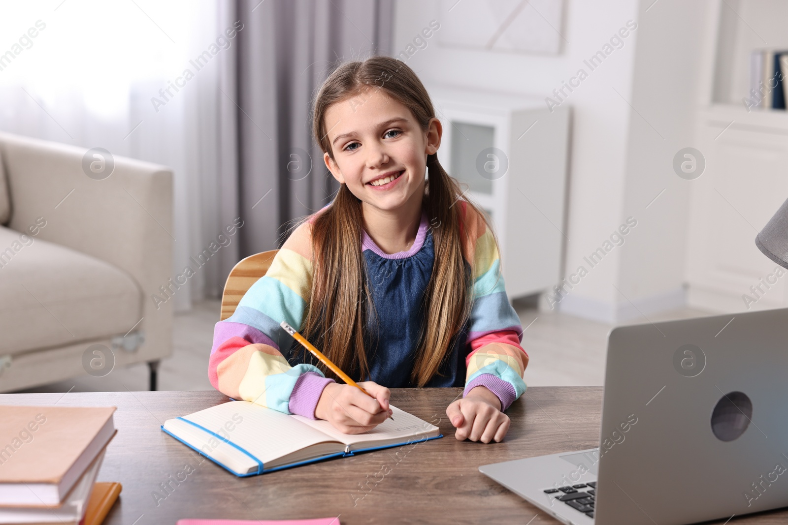 Photo of E-learning. Cute girl taking notes during online lesson at table indoors