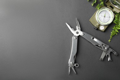 Photo of Compact portable metallic multitool, compass and green leaves on grey background, flat lay. Space for text