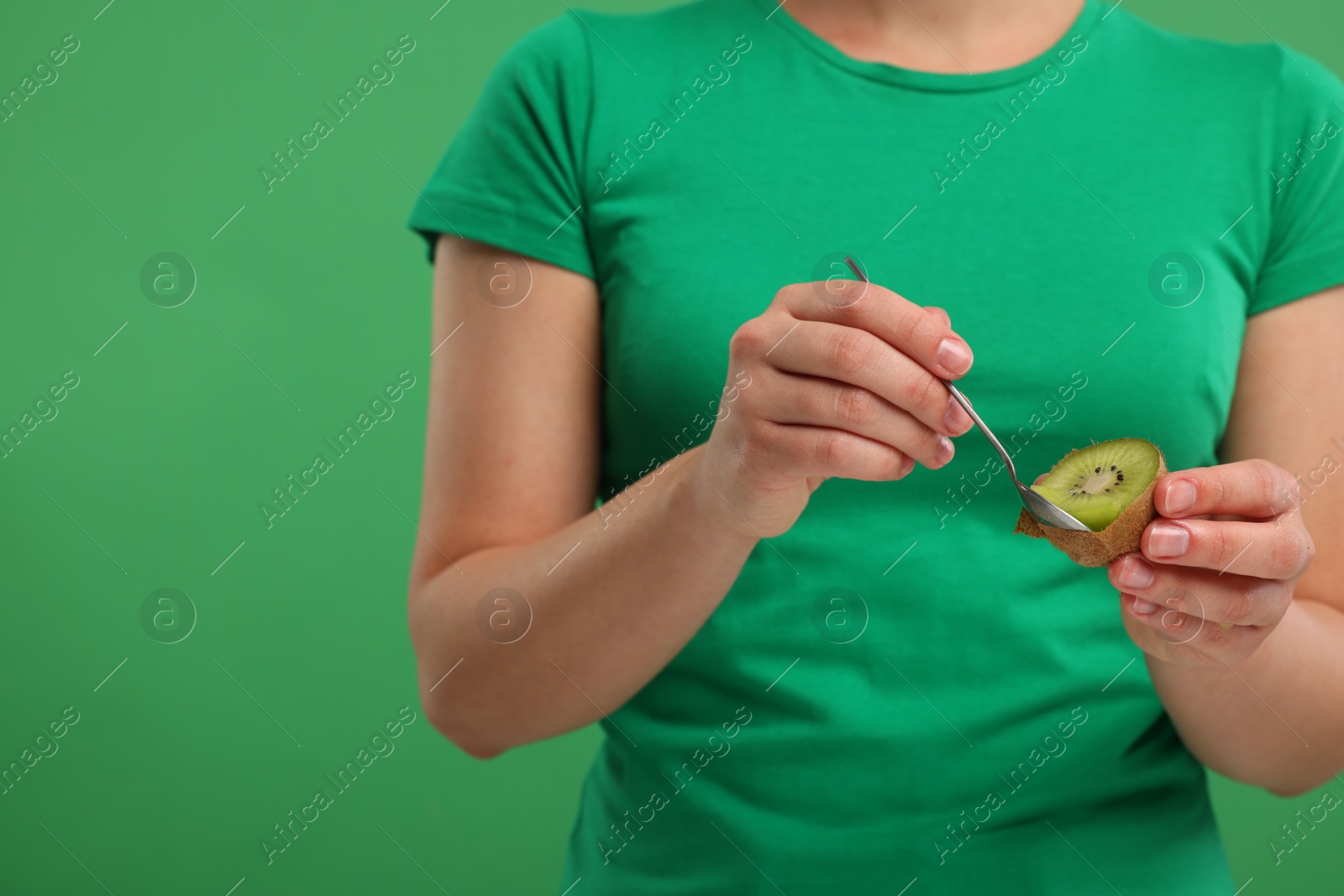 Photo of Woman eating kiwi with spoon on green background, closeup. Space for text