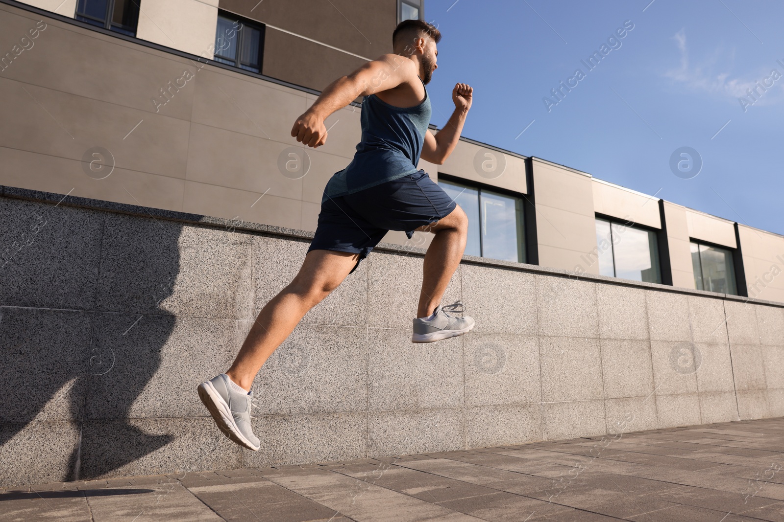 Photo of Young man running near building outdoors, low angle view. Space for text