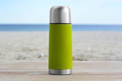 Metallic thermos with hot drink on wooden surface near sea