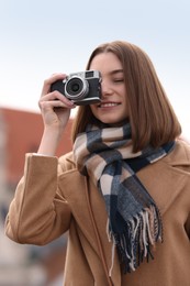 Photo of Beautiful woman in warm scarf taking picture with vintage camera outdoors