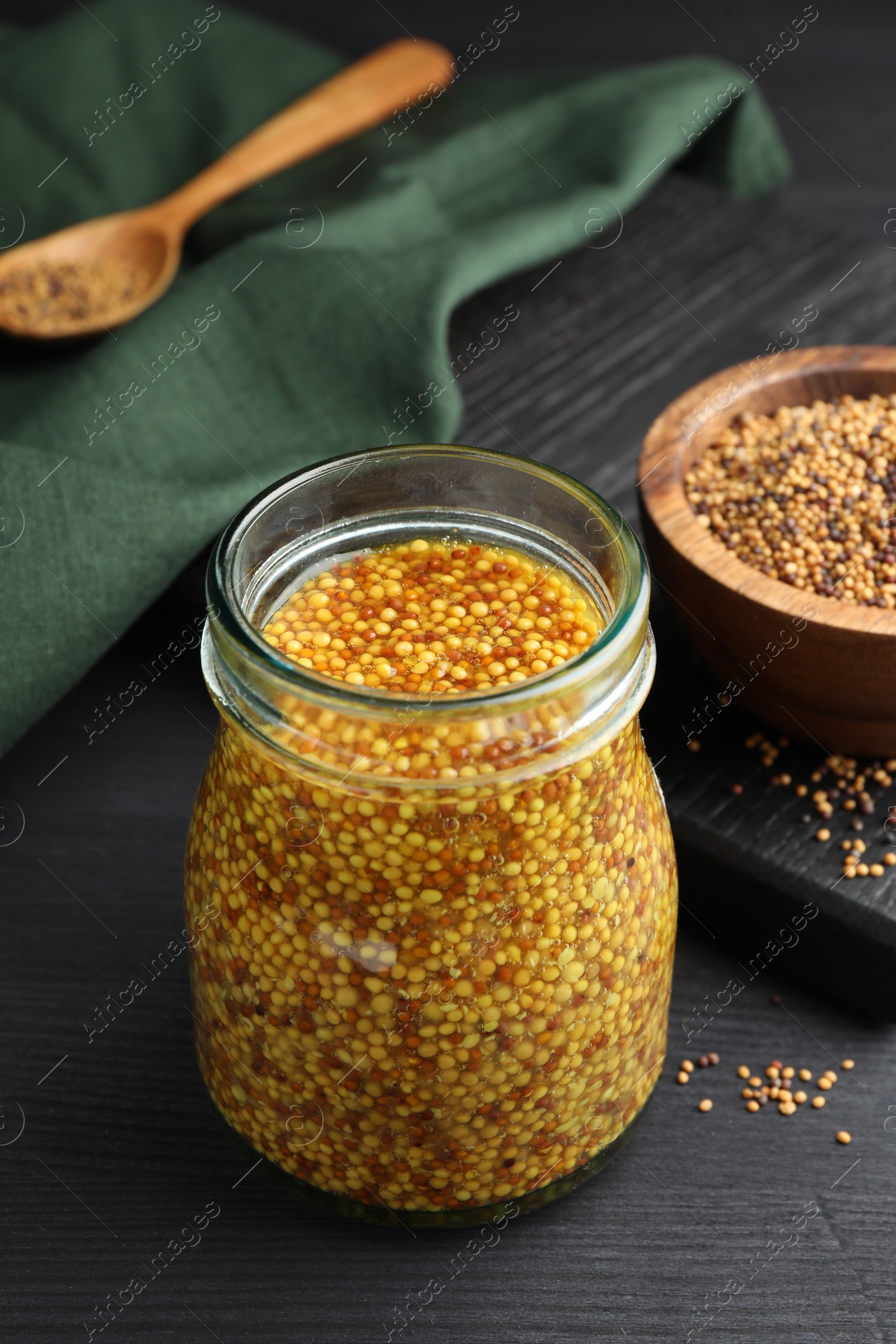 Photo of Whole grain mustard in jar and dry seeds on black wooden table