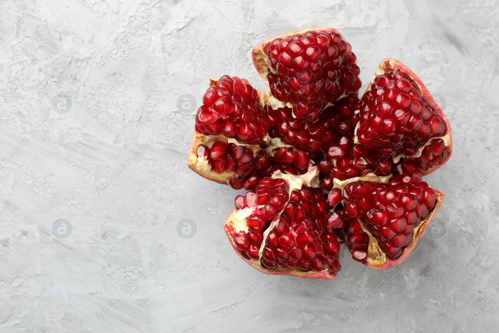 Photo of Cut fresh pomegranate on grey textured table, top view. Space for text