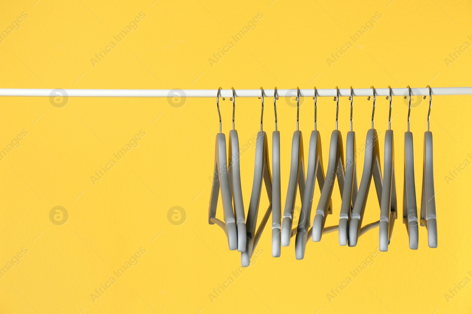 Photo of Metal rack with clothes hangers on color background, space for text