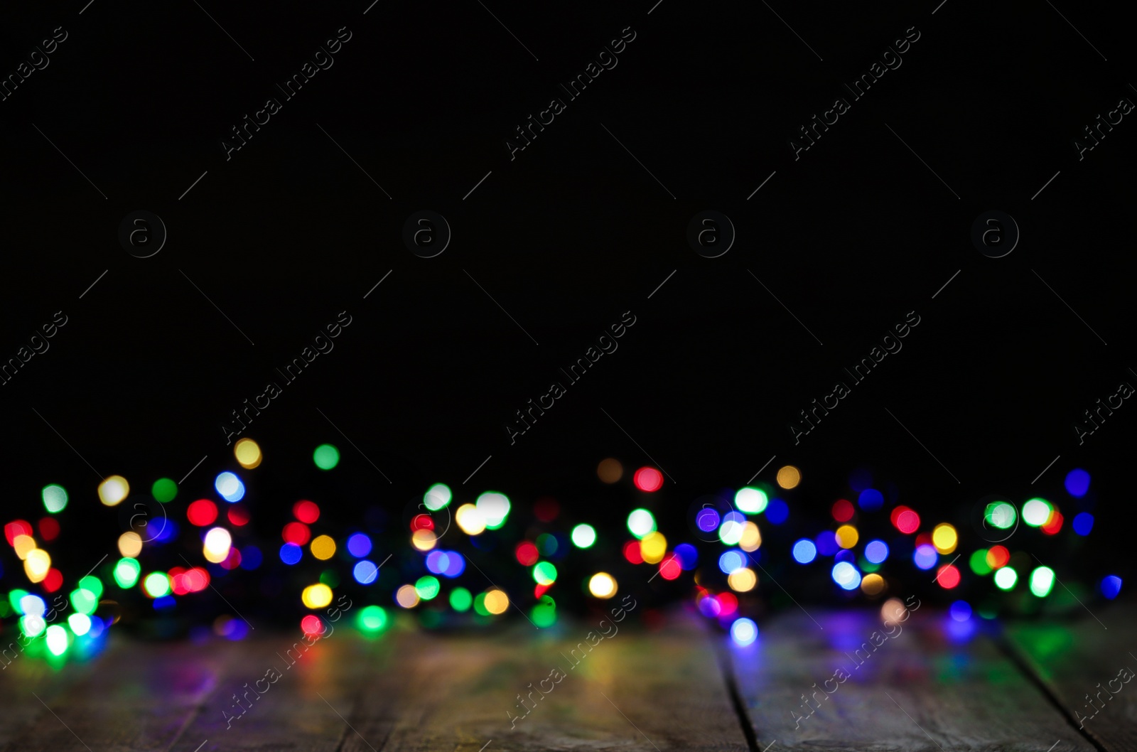 Photo of Colorful Christmas lights on wooden table, blurred view