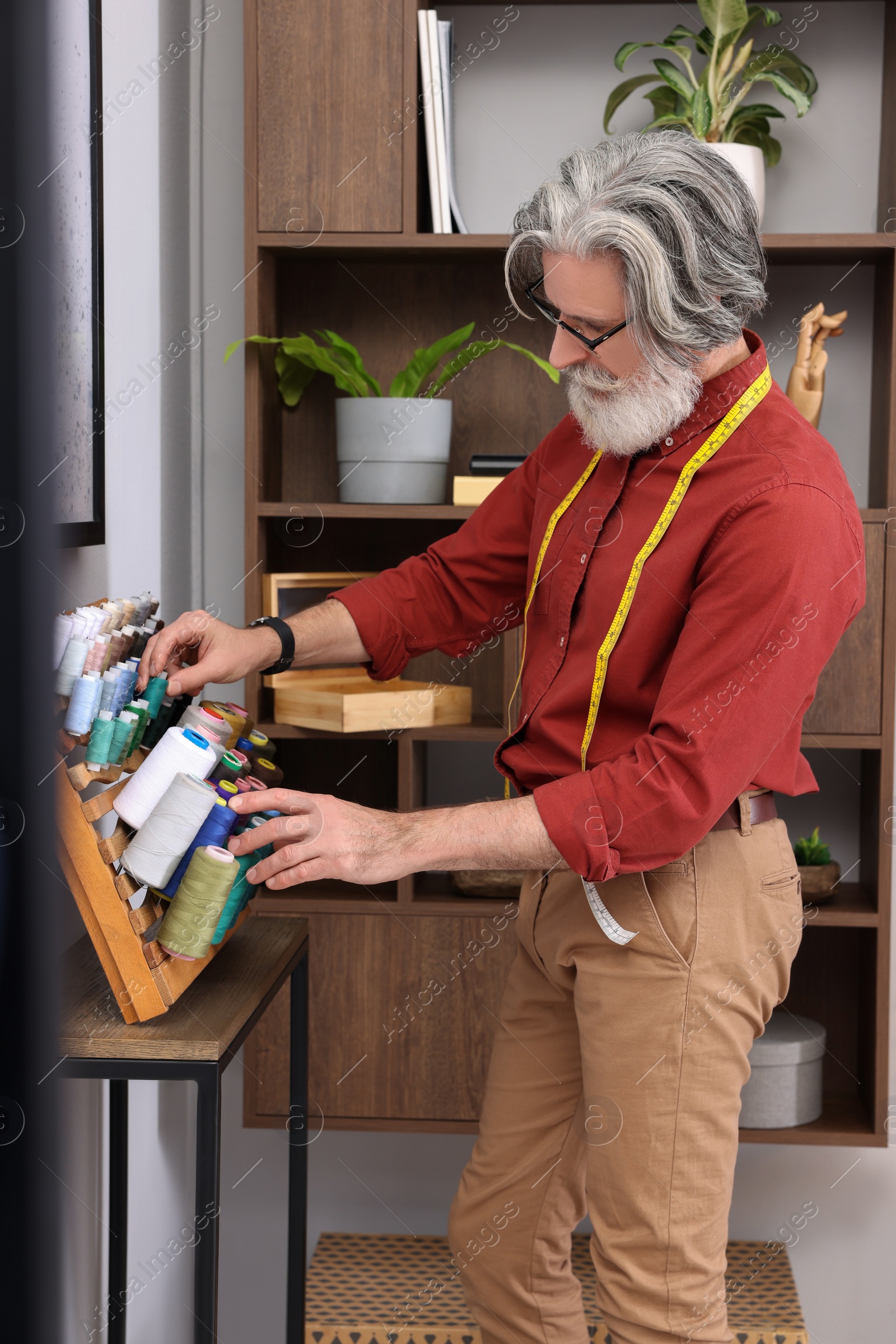 Photo of Professional tailor choosing thread near stand in workshop