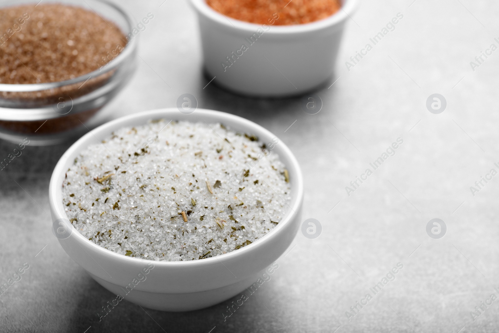 Photo of Different kinds of salt in bowls on grey table, space for text