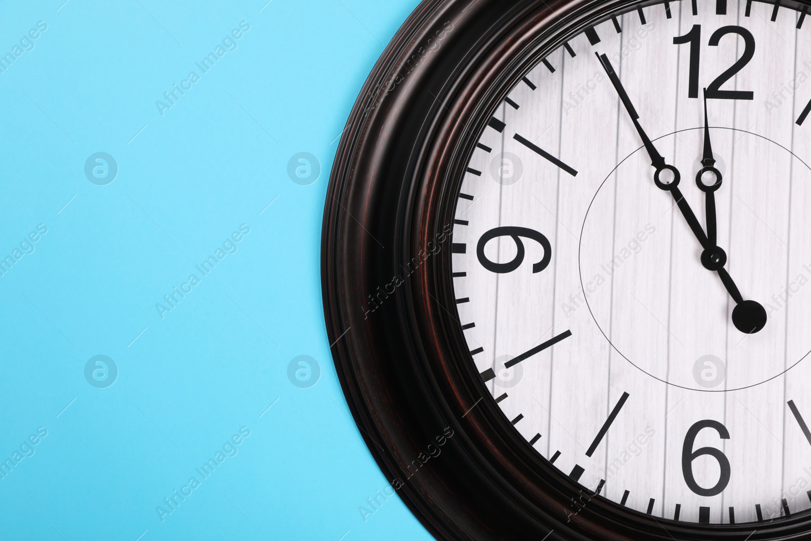 Photo of Stylish wall clock showing five minutes until midnight on turquoise background, top view with space for text. New Year countdown