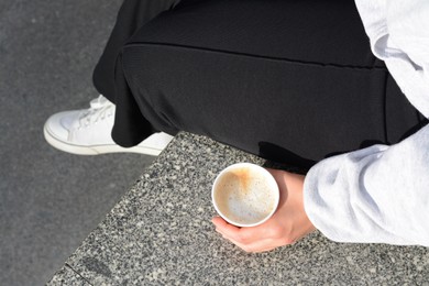 Woman sitting with cardboard cup of coffee outdoors, above view