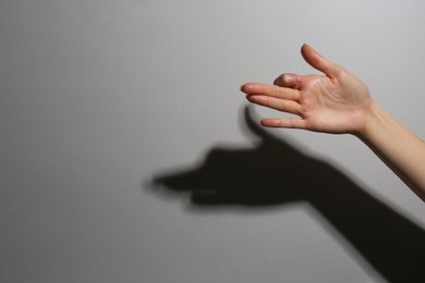 Shadow puppet. Woman making hand gesture like dog on grey background, closeup. Space for text