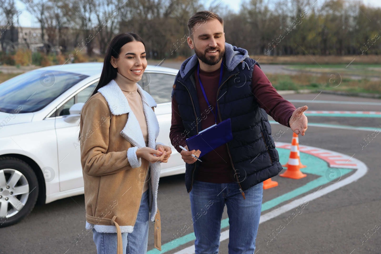 Photo of Young woman with instructor near car at driving school test track