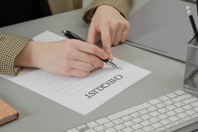 Woman filling Checklist at light grey table, closeup