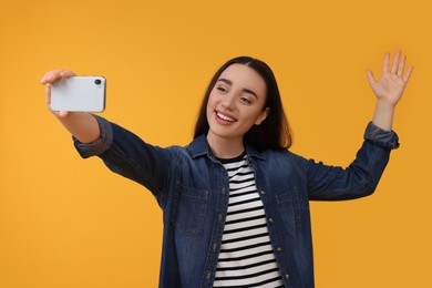 Photo of Smiling young woman taking selfie with smartphone on yellow background