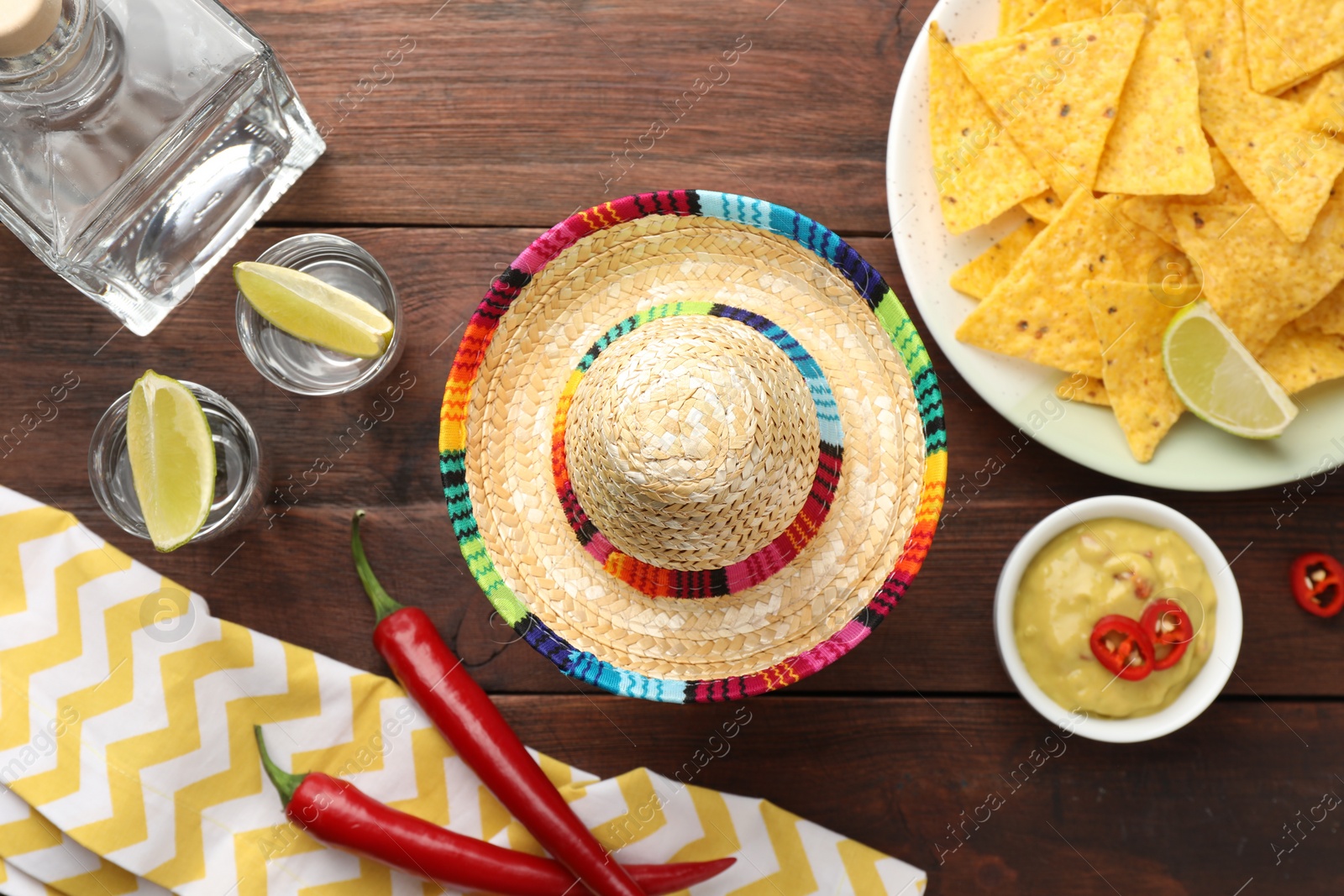 Photo of Mexican sombrero hat, tequila with lime, chili peppers, nachos chips and dip sauce on wooden table, flat lay