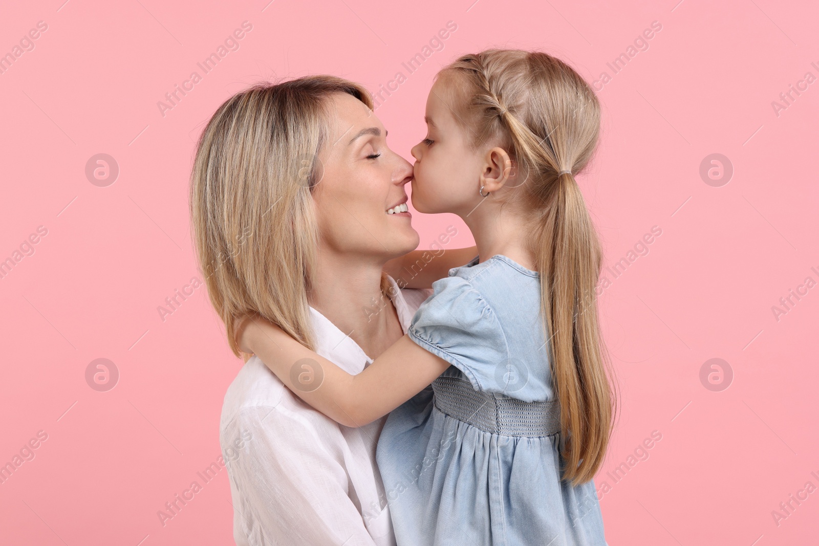 Photo of Daughter hugging and kissing her happy mother on pink background