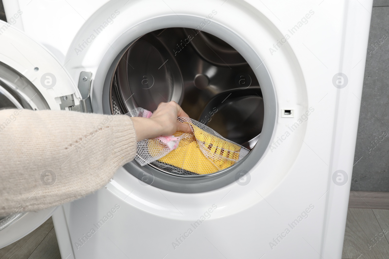 Photo of Woman putting stylish sneakers into washing machine, closeup