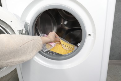 Woman putting stylish sneakers into washing machine, closeup