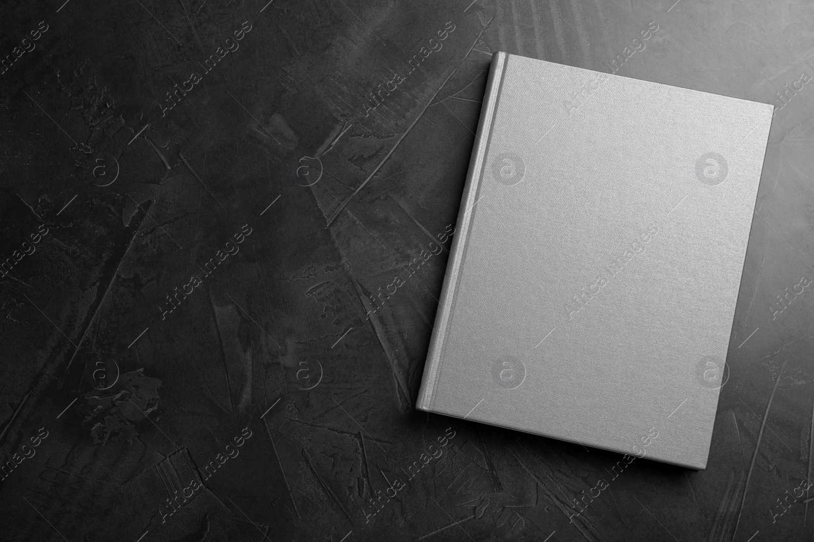 Photo of Closed grey book with hard cover on black table, top view. Space for text