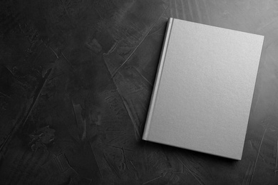 Photo of Closed grey book with hard cover on black table, top view. Space for text