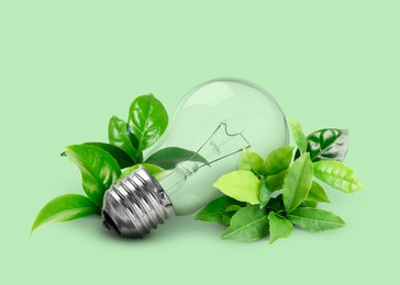 Image of Saving energy, eco-friendly lifestyle. Light bulb and fresh leaves on green background