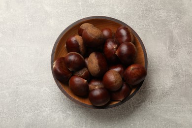 Photo of Roasted edible sweet chestnuts in bowl on light grey table, top view