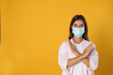 Photo of Woman in protective mask showing stop gesture on yellow background, space for text. Prevent spreading of coronavirus