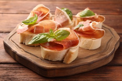 Photo of Board of tasty sandwiches with cured ham and basil leaves on wooden table, closeup