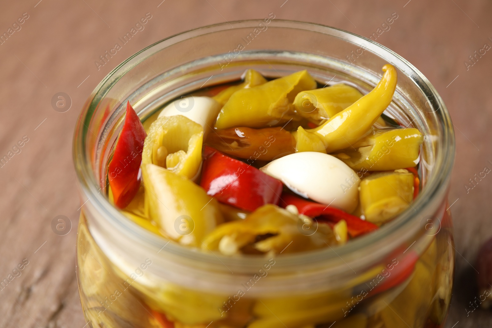 Photo of Glass jar with pickled peppers on brown table, closeup