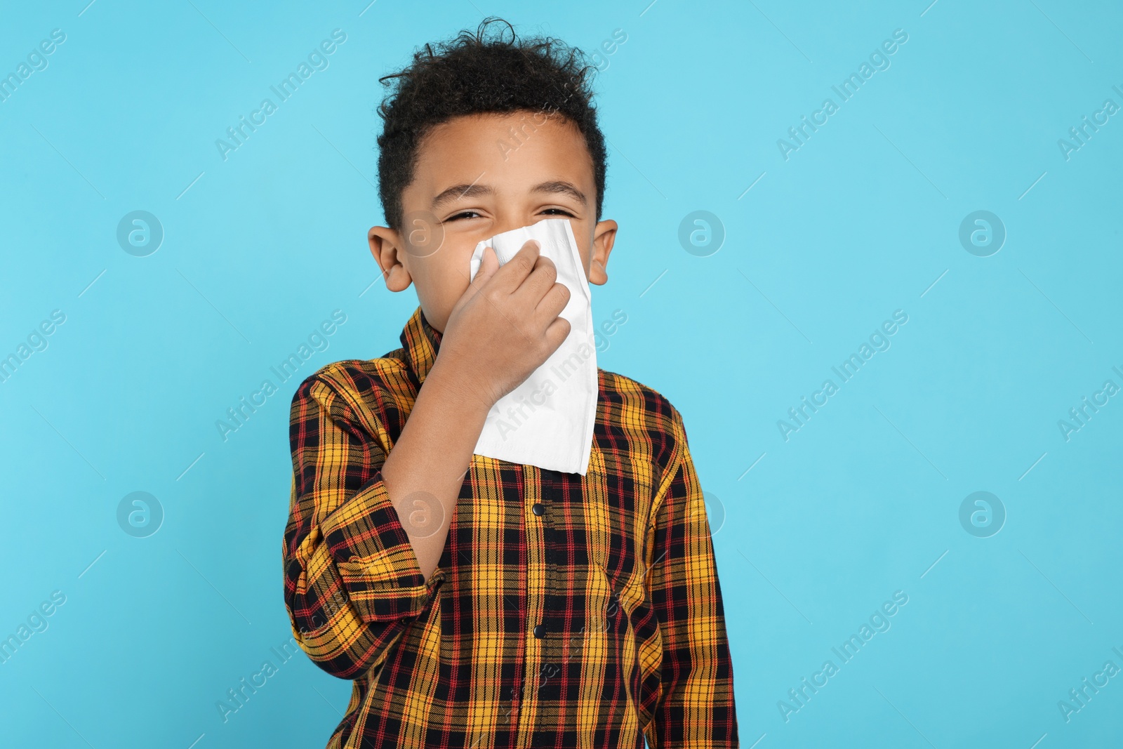 Photo of African-American boy blowing nose in tissue on turquoise background. Cold symptoms