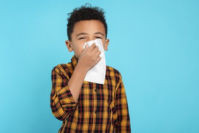African-American boy blowing nose in tissue on turquoise background. Cold symptoms